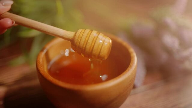 A person is dipping wooden spoon in honey. Golden fresh honey is pouring from stick. Organic beekeeping. Concept of healthy organic food and sweet meals.