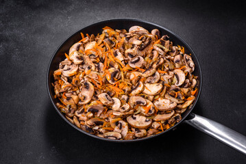 Fried champignons with carrots, onions and spices in a pan against a dark concrete background