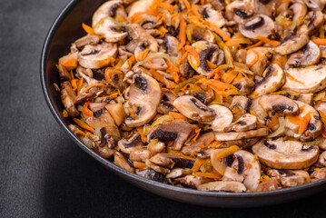 Fried champignons with carrots, onions and spices in a pan against a dark concrete background