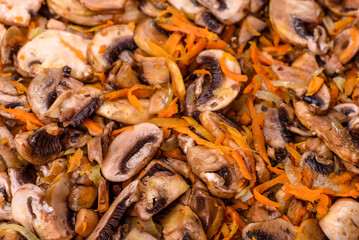 Fried champignons with carrots, onions and spices in a pan against a dark concrete background