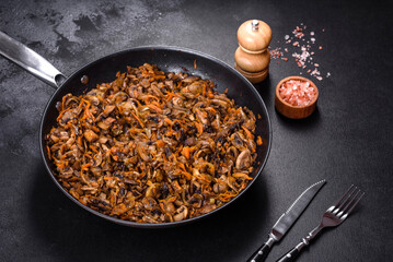 Fried champignons with carrots, onions and spices in a pan against a dark concrete background