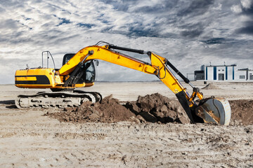 Obraz premium A powerful caterpillar excavator digs the ground against the evening sunset. Earthworks with heavy equipment at the construction site. Excavator in contrast against the sky.