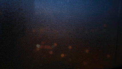 Close-up of window with raindrops on blurred background of lights. Concept. Dim lights shine through dark window blurred by raindrops