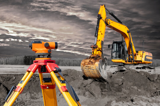 Modern level for geodesy at a construction site. Surveyors ensure precise measurements before undertaking large construction projects. Excavator on the background of the sunset sky. contrast image.