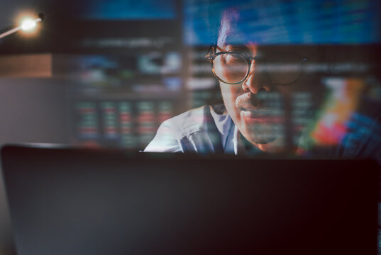 Trader wearing eyeglasses working on laptop analyzing online stock market with reflection.