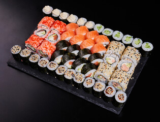 Large set of various sushi rolls with fresh different fillings on a black stone plate.