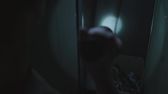 Rear of soldier with shaved head holding flashlight, looting in abandoned dark changing room, finding still zombie in locker