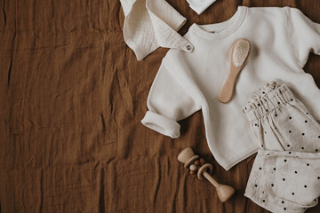 Stylish elegant newborn baby clothes and accessories on neutral brown linen cloth. Sweater, joggers, hat, muslin bib, brush. Online fashion store, online shopping branding concept.