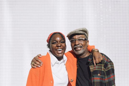 Portrait of cheerful father and daughter with arms around against wall during sunny day