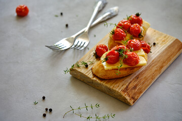 Fried slices of fresh bread with cheese and cherry tomatoes on a wooden board on a gray background. T
