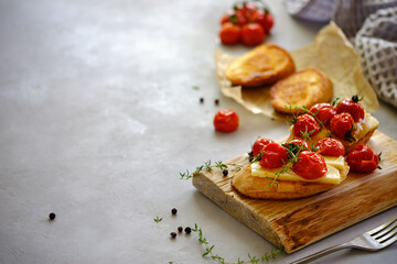 Fried slices of fresh bread with cheese and cherry tomatoes on a wooden board on a gray background. T