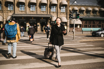 Businesswoman pulling luggage while crossing street in city on sunny day