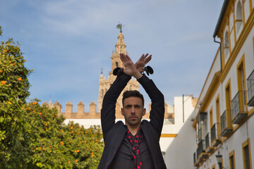 gypsy man dancing flamenco, dressed in black with castanets is posing with his arms up among orange trees and in the background the giralda of seville. Flamenco cultural heritage of humanity - obrazy, fototapety, plakaty