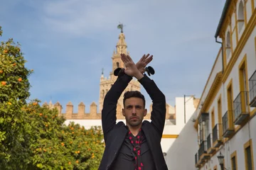 Poster gypsy man dancing flamenco, dressed in black with castanets is posing with his arms up among orange trees and in the background the giralda of seville. Flamenco cultural heritage of humanity © @skuder_photographer