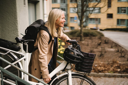 Side view of smiling businesswoman with backpack holding electric bicycle