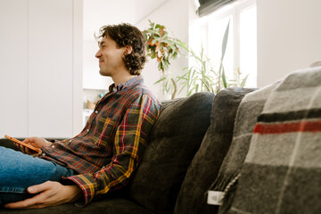 White man smiling and using mobile phone while resting on couch