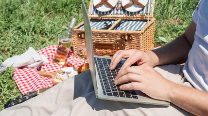 unrecognizable man in white pants outside having picnic and using laptop, working outdoors