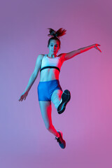 Training in long jump sport. Young girl, female athlete practicing isolated on pink studio background with blue neon filter, light. Concept of action, motion, speed