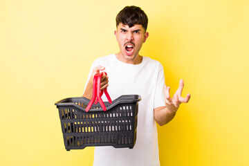 young hispanic man looking angry, annoyed and frustrated. empty shopping basket concept