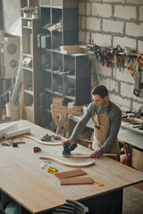 Mood shot of young carpenter working alone in shop and sanding piece of handcrafted furniture - obrazy, fototapety, plakaty