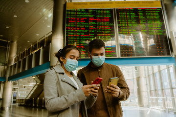 Indian couple wearing face masks using mobile phones at train station