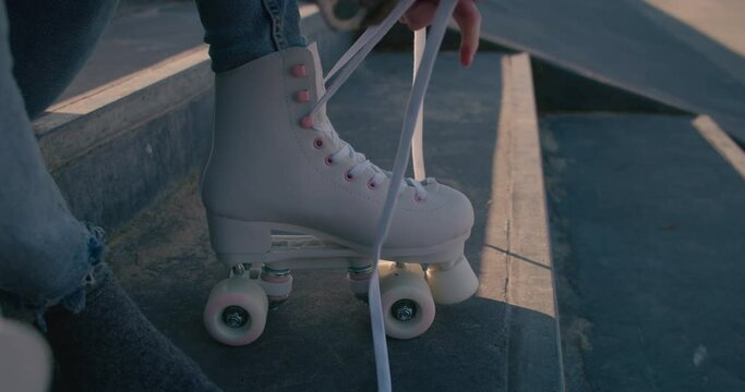 Close up of girl sitting on a step of staircase tying the laces of her skating shoes. Slow motion.