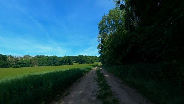 FPV DRONE - REVERSE SHOT flight over dirt road, close to green field