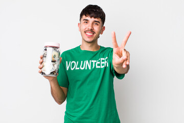 hispanic volunteer smiling and looking happy, gesturing victory or peace. donations concept