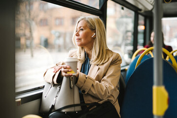 Businesswoman looking through window holding disposable cup while commuting in bus