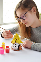 Girl making toys with your own hands, paints a clay house with gouache. Indoors creative leisure for children. Supporting creativity, learning by doing, DIY project, hand craft. Master class of art
