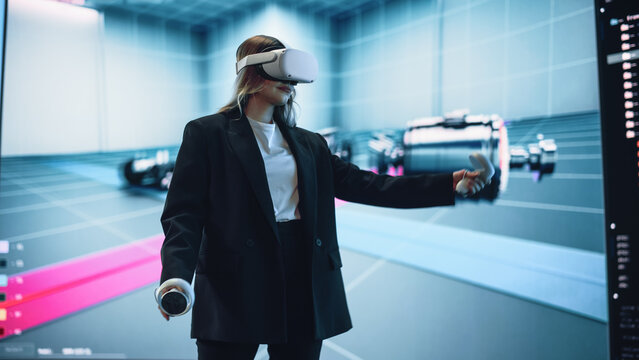 Automotive Engineer Using a VR Software to Showcase Electric Motor and Vehicle Platform in Interactive Environment on a Big Digital Screen. Female Engineer Using Headset and Controllers.