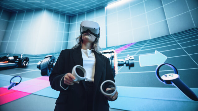 Automotive Engineer Using a VR Software to Showcase Electric Motor and Vehicle Platform in Interactive Environment on a Big Digital Screen. Female Engineer Using Headset and Controllers.