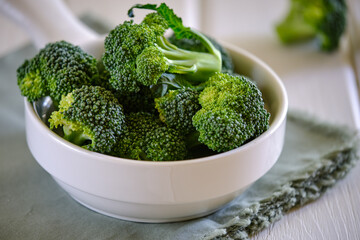 Fresh green broccoli in white bowl on light table..