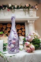 Decorative purple bottle of champagne, with patterns of flowers, candles and flowers, at the festive table for the newlyweds in a cozy restaurant by the fireplace with firewood.