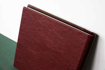 A large expensive premium photo book in a brown leather cover stands against a white wall on a green cloth indoors.
