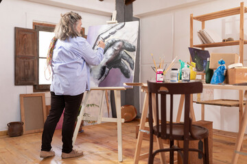 Mature artist woman spends her leisure time developing her painting skills at her workshop