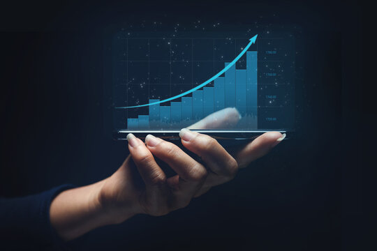 Stock graph market trading concept with digital smart phone on woman hand and digital financial blue chart graphs technology on dark background with copyspace.