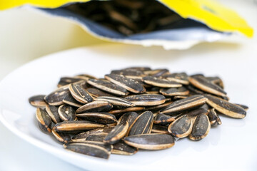 Nutritious sunflower seeds on a white plate in the foreground, poured from bag out of focus in background, selective focus, healthy eating concept