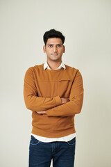 Portrait of young Indian software developer in mustard sweater crossing arms and looking at camera