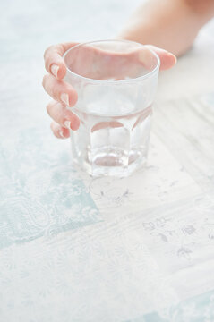 Woman's hand holds a glass of fresh water on a table with a tablecloth. Stay hydrated during the hot days of the year. World Water Day concept.