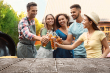 Empty wooden table and blurred view of friends with drinks near barbecue grill outdoors