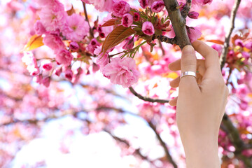 Young woman holding branch of blossoming sakura tree outdoors, closeup. Space for text