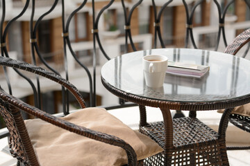 Stylish table with cup of coffee and notebook near comfortable armchair on balcony. Good morning