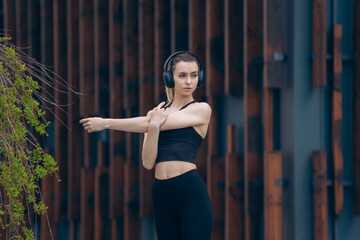 Girl in earphones stretching arms outdoors.