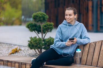 Girl sitting on leg on bench, holding smartphone.