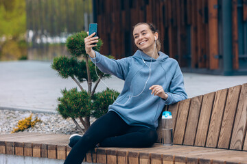 Girl in earphones taking selfie outdoors, bending head.