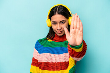 Young hispanic woman listening to music isolated on blue background standing with outstretched hand showing stop sign, preventing you.