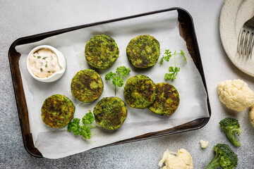 Broccoli and cauliflower green fritters or pancakes with sauce, top view