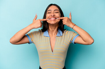 Fototapeta premium Young hispanic woman isolated on blue background smiles, pointing fingers at mouth.