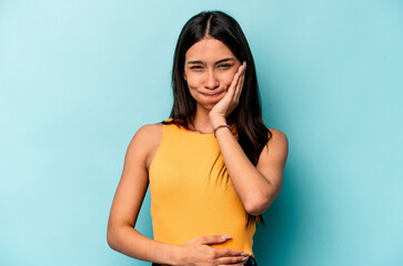 Young hispanic woman isolated on blue background blows cheeks, has tired expression. Facial expression concept.